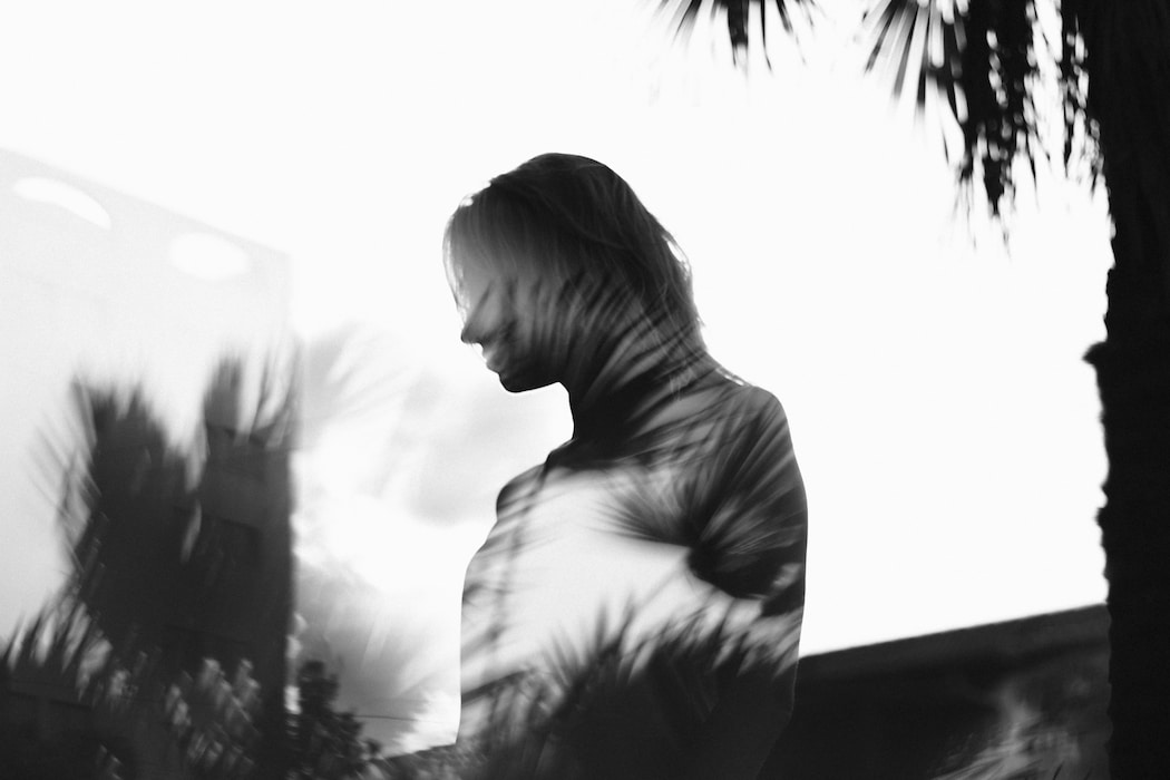 A moody double-exposure of a woman superimposed over palm fronds